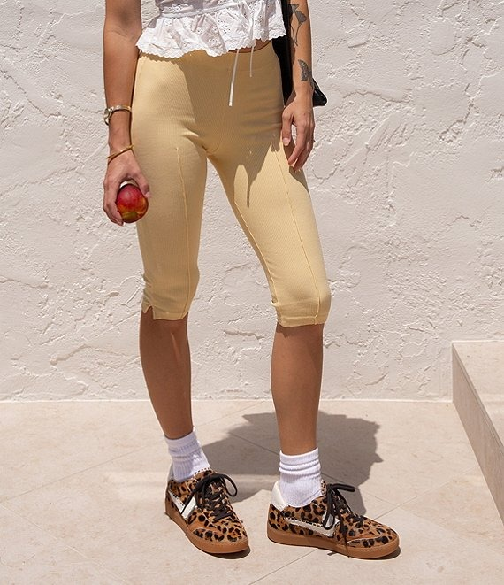 Person in casual capri leggings, holding an apple, wearing leopard print sneakers and a white frilly tank top
