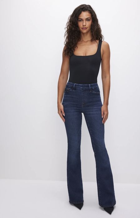 A person modeling dark wash bootcut jeans with a black tank top.