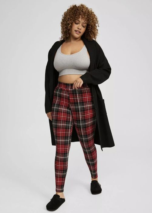 A person wearing plaid leggings, a gray crop top, and a long black cardigan, striking a stylish casual pose.