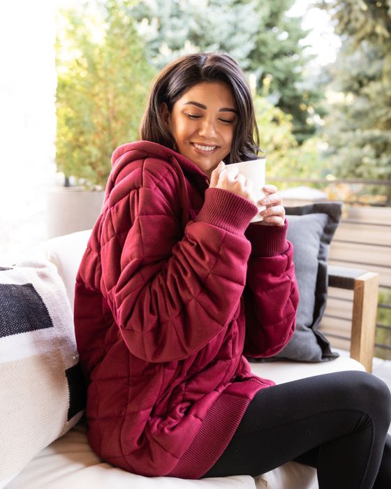 A person enjoys a tranquil moment outdoors, wrapped in a cozy quilted hoodie while sipping from a mug