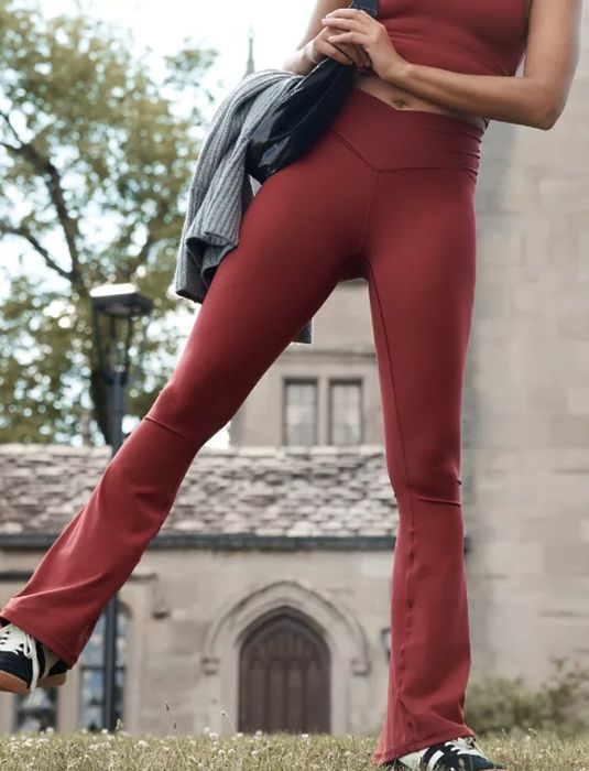 A model in a courtyard, kicking her right leg to the side, wearing red leggings and a matching crop top.