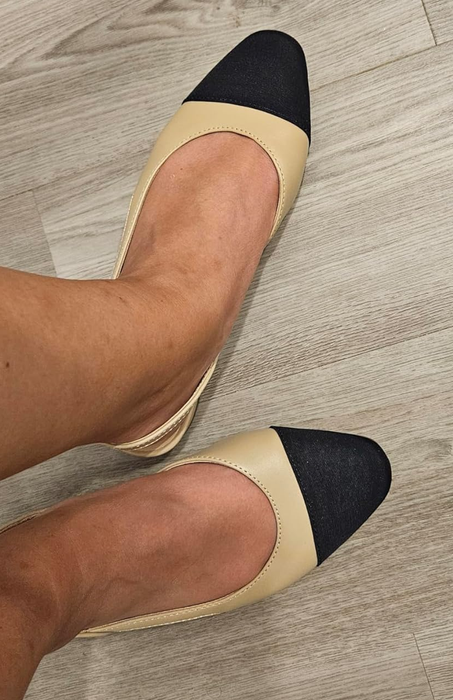 Beige and black slingback flats worn on a wooden floor