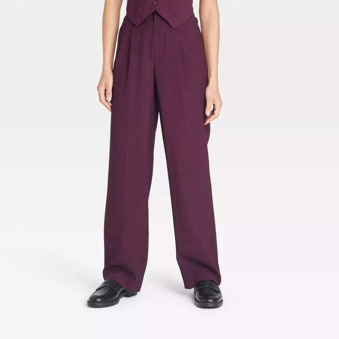 An individual styled in wide-leg pants, a buttoned vest, and classic black loafers.