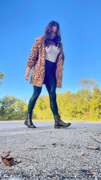 A person walking outside, dressed in a leopard-print coat, white top, black pants, and boots, featured in a shopping article.