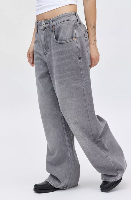 A person rocks high-waisted, wide-leg jeans paired with black shoes, showing off a tattooed arm. A fashionable, casual look perfect for shopping.