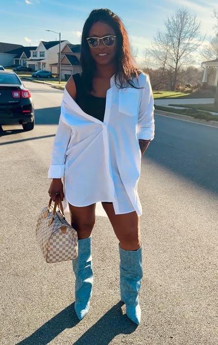 A person outdoors wearing an oversized white shirt, black top, knee-high boots, and sunglasses