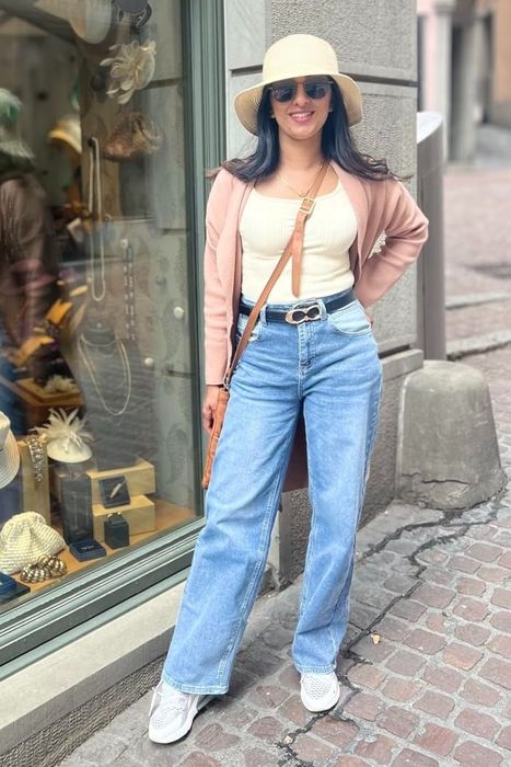 A reviewer wearing wide-leg jeans, a hat, and sunglasses, stands by a shop display on a charming cobblestone street.