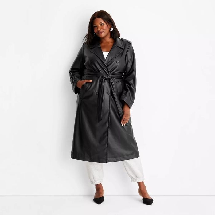 A person styled in a long black trench coat paired with white pants and black heels, ideal for a fashion feature on chic clothing styles