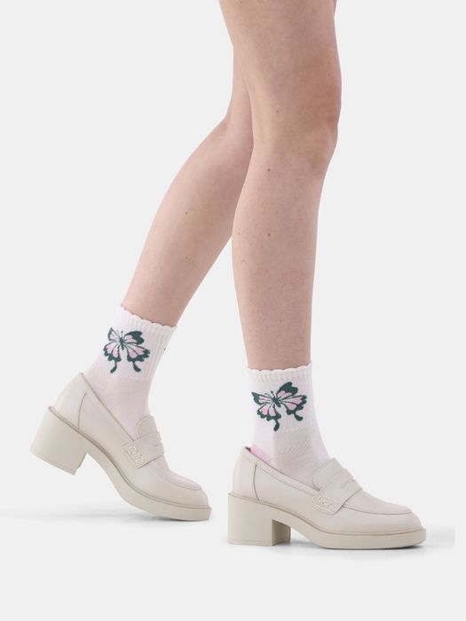 A fashion model showcasing white platform loafers paired with socks featuring a floral motif