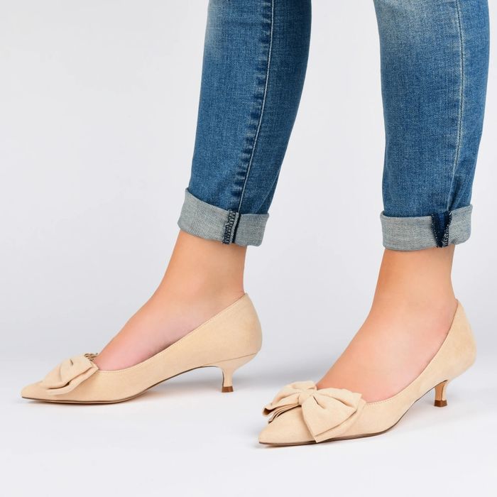 An individual styled in rolled-up jeans paired with beige kitten heels featuring elegant bows