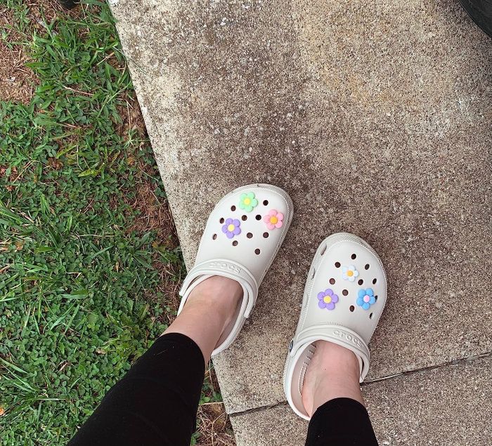 A reviewer wearing white Crocs decorated with flower charms
