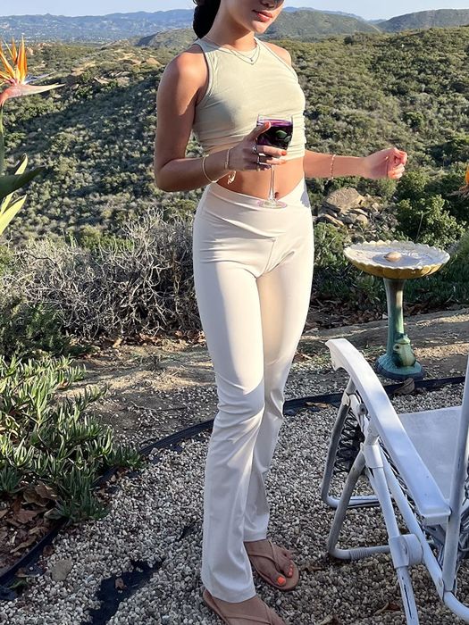 A reviewer standing outdoors, holding a glass of wine while wearing white pants.