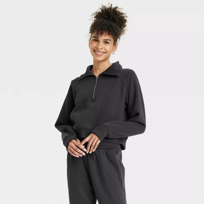 A person is sporting a casual black, long-sleeve zip-up hoodie and matching joggers, smiling at the camera.