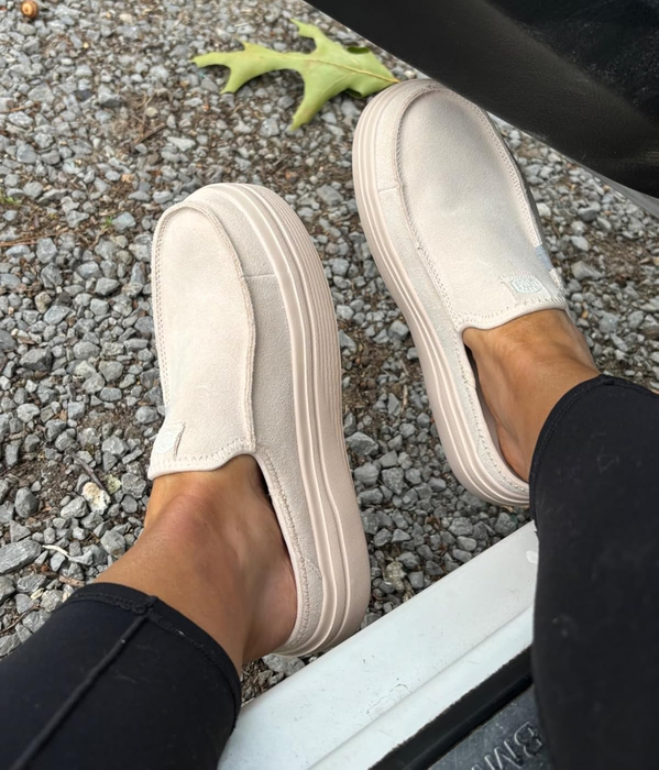 Person wearing light slip-on sneakers with thick soles, seated in a vehicle with one foot resting outside