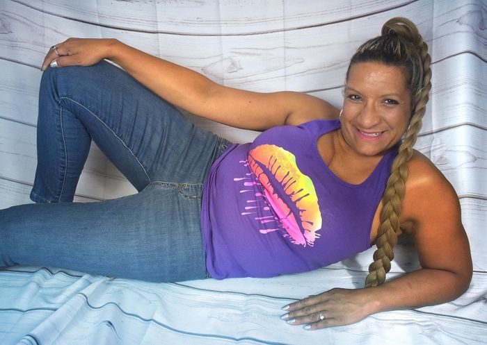 A reviewer grinning, relaxing in jeans and a purple sleeveless top featuring a bold lip graphic.