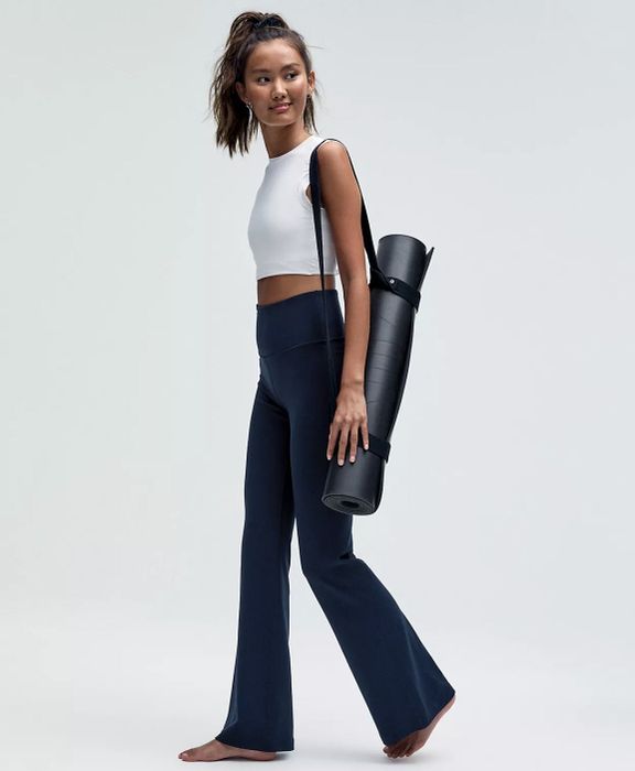 A model in activewear with a yoga mat bag slung over their shoulder, posing against a plain background, wearing the blue yoga pants.