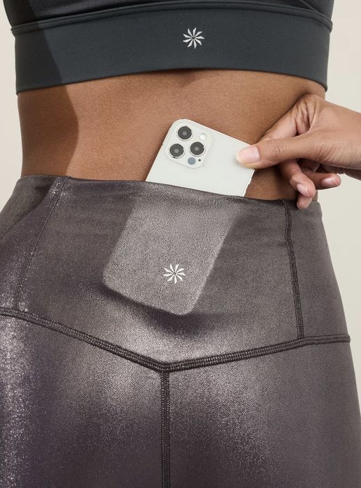 A person sporting glossy athletic leggings, slipping a smartphone into a concealed waistband pocket