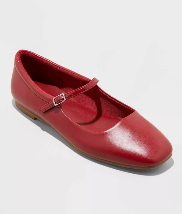 Red leather Mary Jane flat shoe with a small buckle strap, photographed against a white backdrop