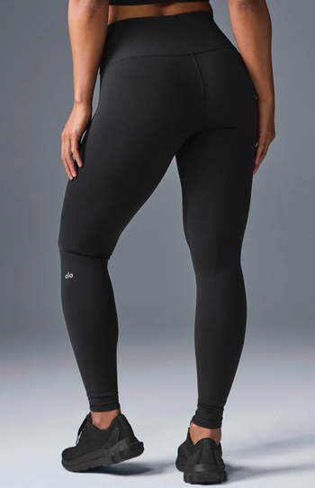 A person wearing black high-waisted leggings and black sneakers, modeling activewear for a shopping article.