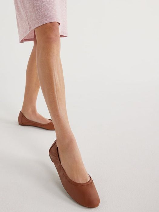 A close-up shot of someone wearing flat brown shoes paired with a pink skirt, showcasing the lower legs