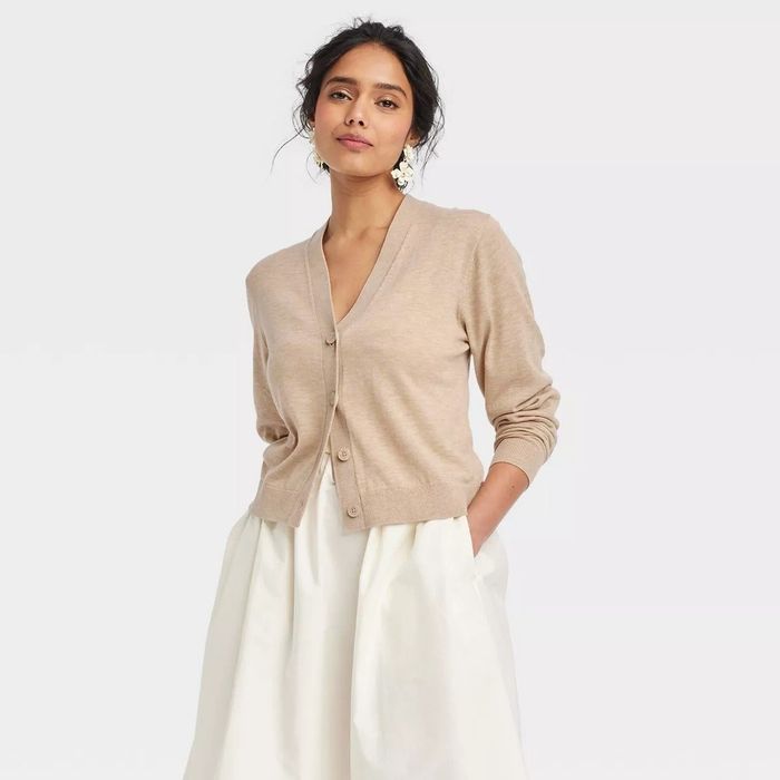 A person styled in a beige button-up cardigan and a white skirt