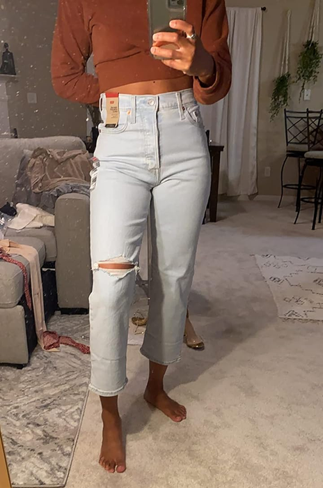 A reviewer showcasing the front of the high-rise jeans in shaded, space ripple lighting.