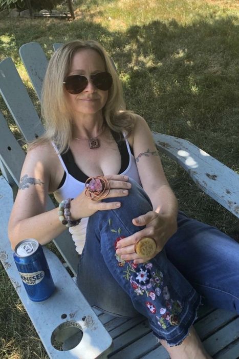 A reviewer sitting outside in a lawn chair, lifting one leg to show off the floral embroidery on her bell-bottoms.