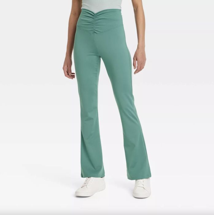 A person styled in a sleeveless top, teal high-waisted flared pants, and white sneakers