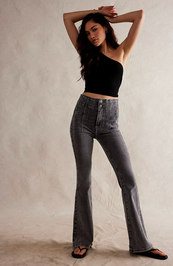 A model in high-waisted flared jeans and a sleeveless top raises their arms in a pose.