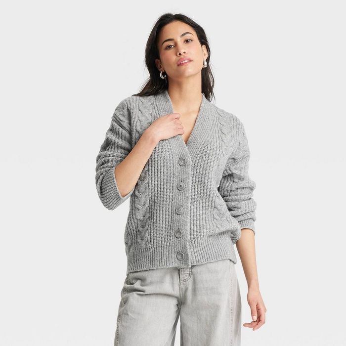 Person wearing a textured knit cardigan and casual pants, posing confidently against a plain backdrop