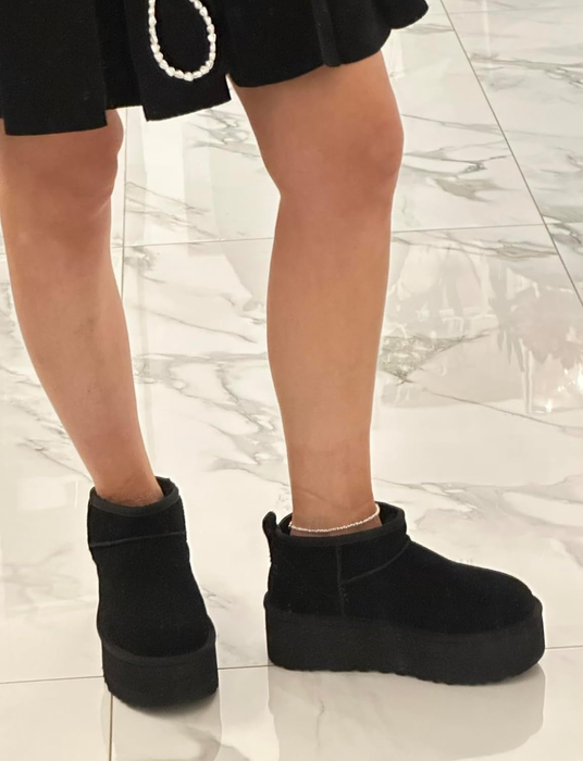 A person wearing stylish black platform boots, standing on a marble floor