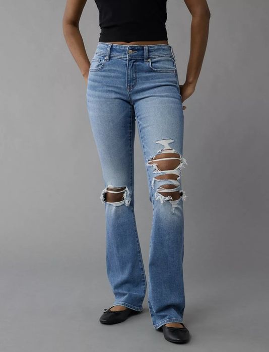 A person modeling ripped jeans and a black top, posed against a simple background.