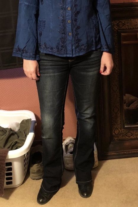 A reviewer showcasing dark blue curvy bootcut jeans, paired with boots and a blouse.