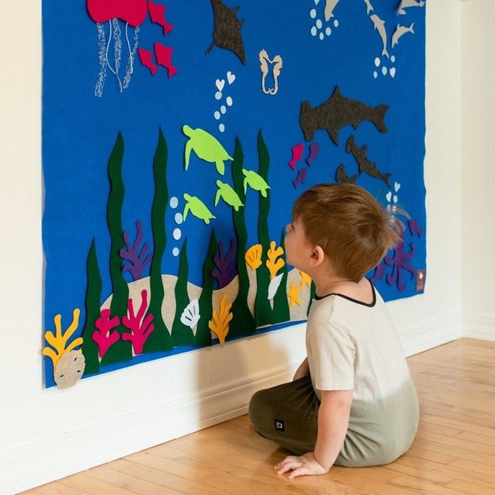 A child is engaged in play, interacting with a textured wall that resembles the ocean's floor, filled with vibrant colors and sea-like elements.