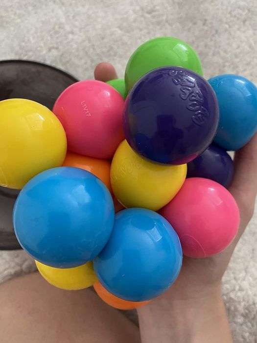 A hand holding a bunch of colorful interlinked plastic spheres, resembling a sensory or stress-relief toy