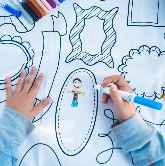 A child busy drawing on a frame-patterned color-in tablecloth.