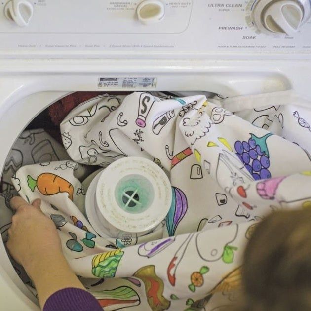 A person tossing the colorful tablecloth into the washing machine.