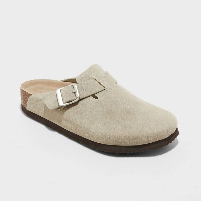 A beige slip-on clog with a strap and buckle, set against a white background. It features a cushioned sole and a suede-like texture for added comfort.