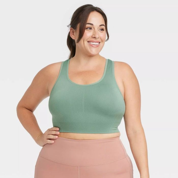 A woman in a green sports bra and pink leggings, smiling, showcasing activewear
