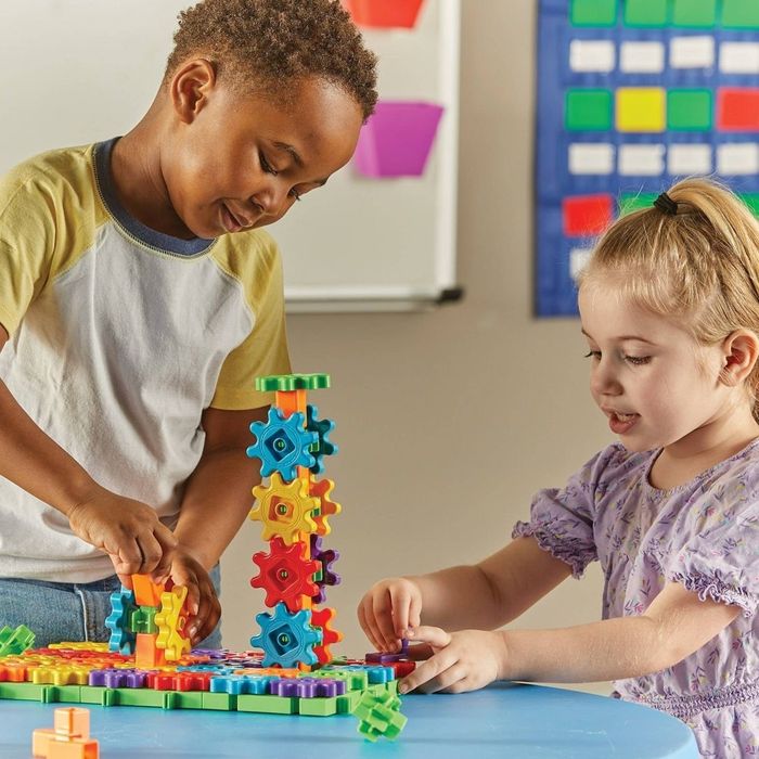 Two kids deeply focused on building a colorful gear structure together at a table, showcasing teamwork and creativity