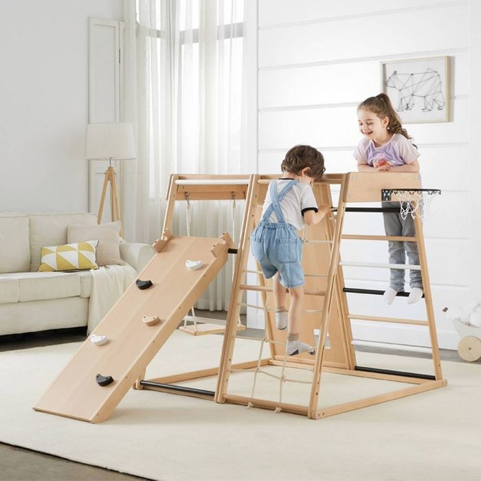 Kids playing on an indoor wooden climbing set complete with a slide and rope ladder, set in a stylish living room