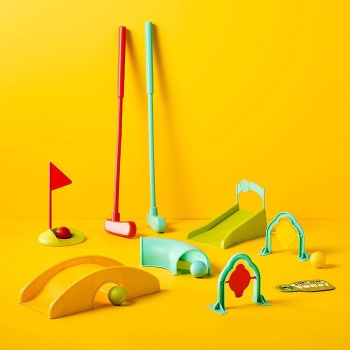 A mini golf set featuring vibrant clubs, balls, flags, and obstacles, arranged on a neutral background and perfect for indoor fun