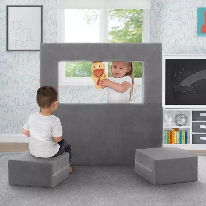 Two children enjoy a puppet theater crafted from foam blocks in a vibrant playroom setting