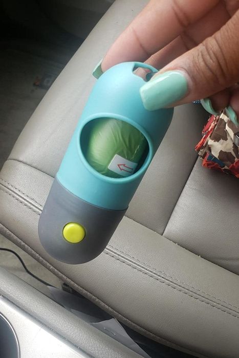 Reviewer photo of a hand holding the blue and gray poop bag dispenser, filled with bags