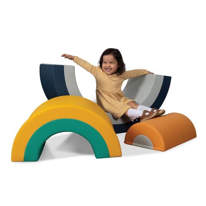 A child in a striped dress joyfully plays on vibrant, arch-shaped foam toys, captured in a playful moment