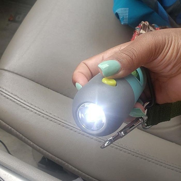 The same reviewer pressing the yellow button on the dispenser to activate the flashlight at its base