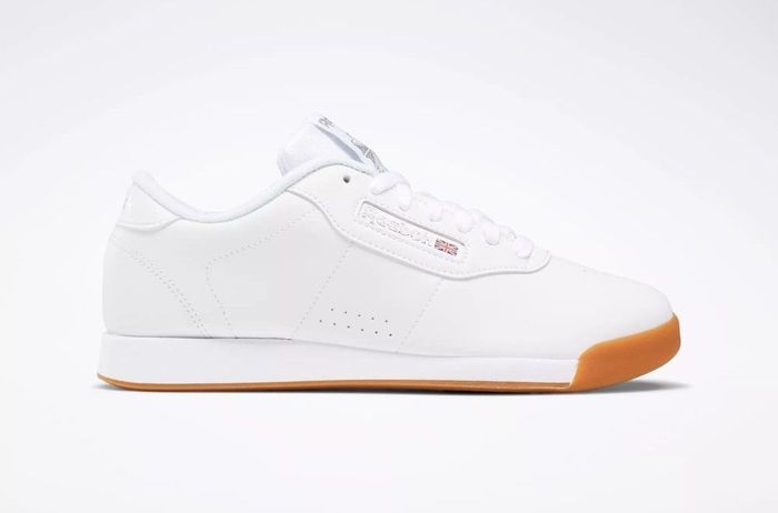 White low-top sneakers with a clean, minimalist design, featuring a gum sole. Primarily intended for casual and daily wear.