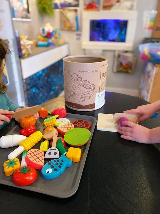 A reviewer’s photo showing a child slicing a pretend wooden vegetable with a tray of pretend food placed on the table.
