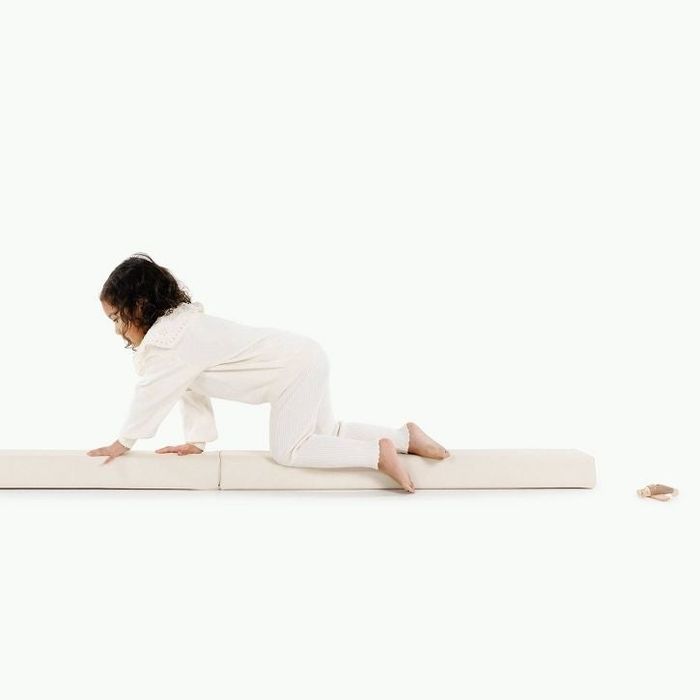 A child in comfortable pajamas crawls on a long cushioned mat, with a small toy close by. Ideal for highlighting kids’ play or sleep-related products