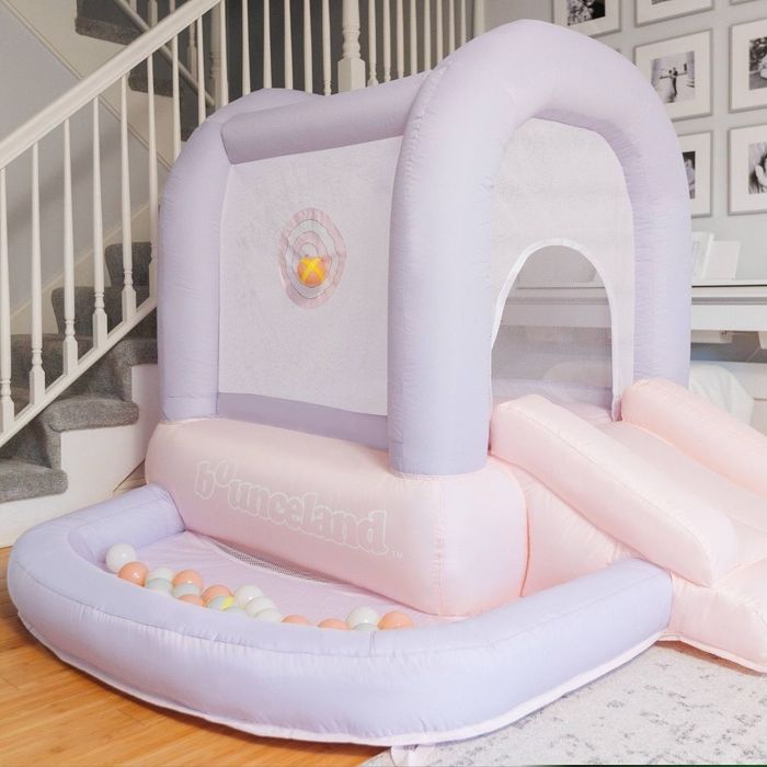 An inflatable indoor bounce house complete with a slide and ball pit, set up in a contemporary living room. Ideal for kids’ play and recreational activities